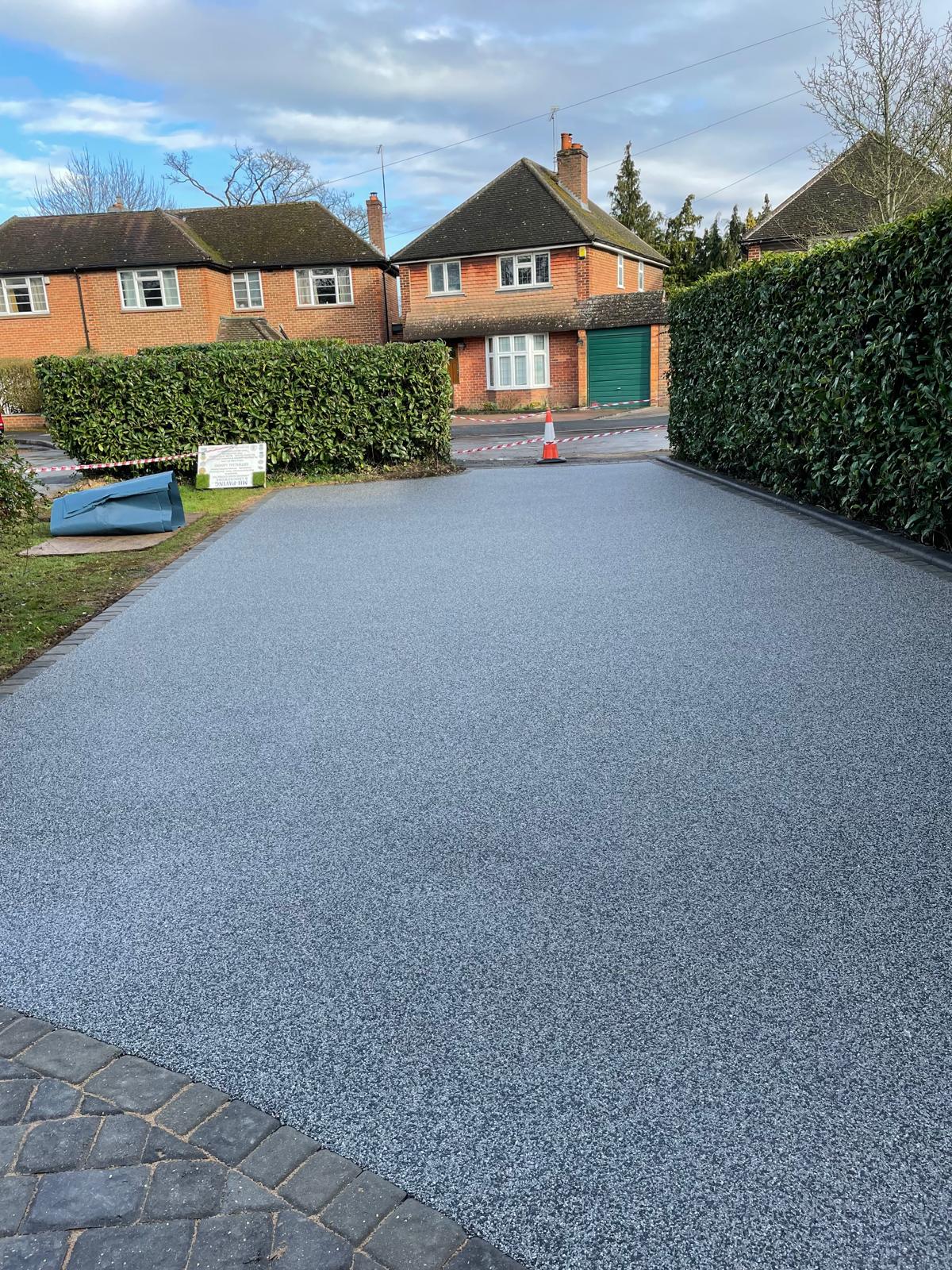 Silver-grey resin-bound driveway with charcoal block border between mature hedging