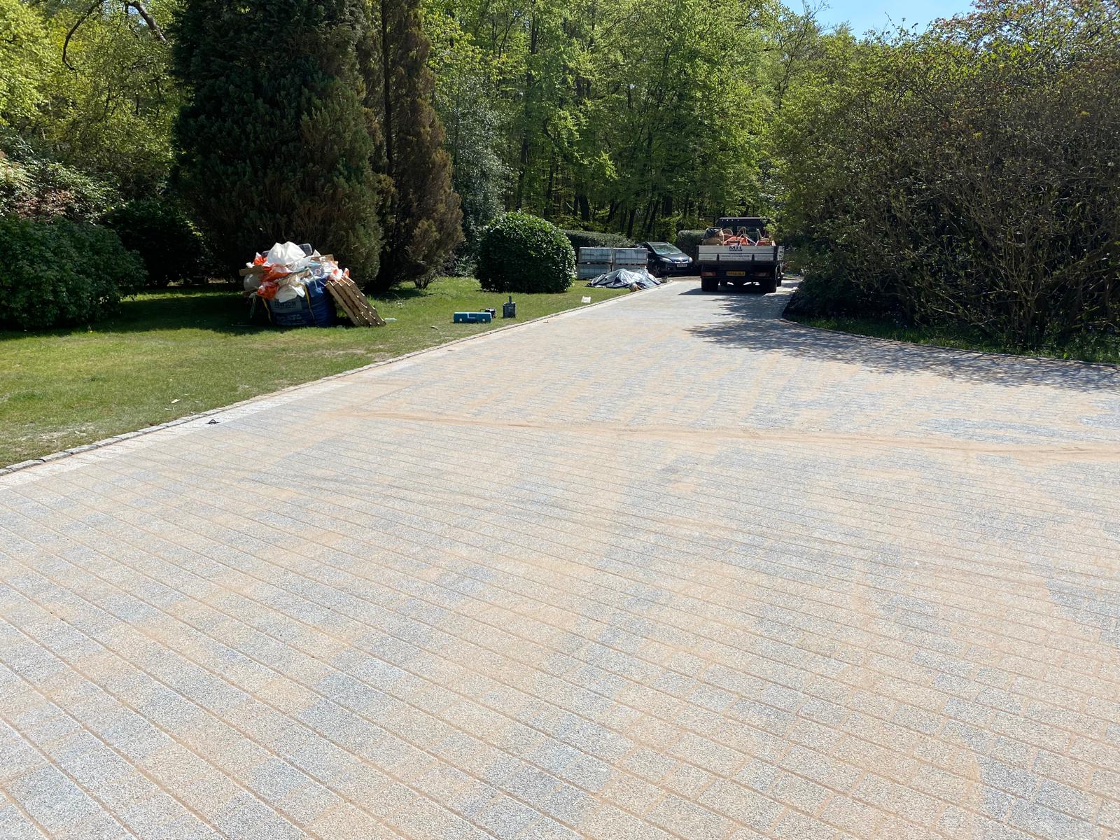 Wide granite block-paved driveway with jointing sand and M H Paving tipper truck in a woodland setting
